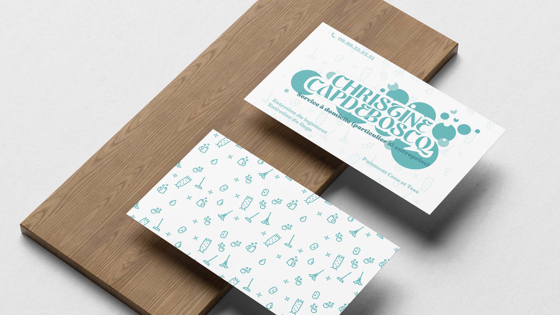 Deux cartes de visites blanches et turquoise sur une planche en bois